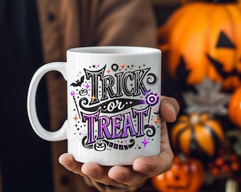 May include: White ceramic mug with the words "Trick or Treat" in a decorative, purple and black font. The mug has a handle and is decorated with bats, stars, and a jack-o'-lantern. The mug is held in a person's hand, with pumpkins in the background.