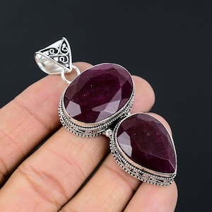 May include: A silver pendant with two large, faceted, dark red ruby stones. The pendant has an intricate, filigree design around the stones.
