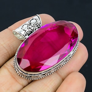 May include: A silver pendant featuring an oval-shaped, faceted, pink gemstone. The pendant has an ornate, silver bail.