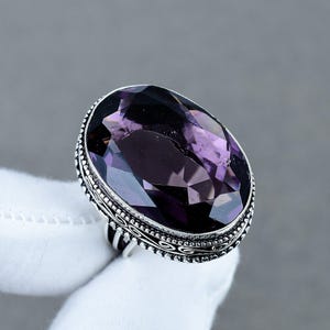 Pode incluir: Um anel com uma grande pedra preciosa de ametista roxa profunda, de corte oval, montada numa banda de prata. A cravação de prata apresenta um trabalho de metal texturizado e intrincado com uma borda de contas em torno da pedra.