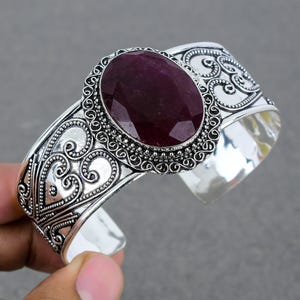 Może przedstawiać: Srebrna bransoletka z ozdobnym wzorem i dużym, owalnym, ciemnofioletowym kamieniem szlachetnym.