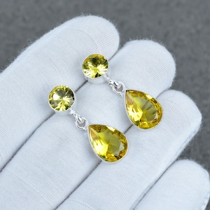 May include: A pair of drop earrings featuring faceted yellow gemstones. Each earring consists of a round-cut stone at the top connected by a silver link to a larger, pear-shaped yellow gemstone dangling below, showcasing a bright, translucent hue.