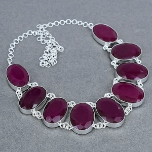 May include: A silver chain necklace with seven oval-shaped, deep purple gemstones. The necklace is made of sterling silver and features a delicate chain.