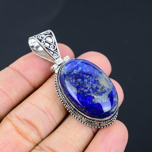May include: A silver pendant with a large oval lapis lazuli stone. The stone is a deep blue with flecks of gold pyrite. The pendant has an intricate silver design around the stone.