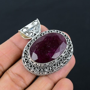 May include: A silver pendant featuring an oval ruby gemstone. The pendant has a filigree design around the gemstone.