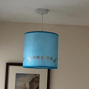 May include: A light blue lampshade with a silver dandelion design. The lampshade is hanging from a white ceiling fixture.