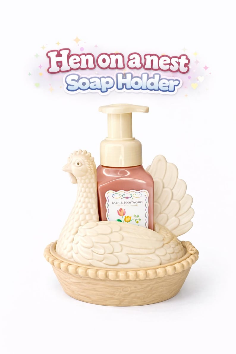 以下が含まれることがあります： クリーム色のニワトリ型のソープホルダーとピンク色のソープディスペンサー。ソープディスペンサーには「Bath & Body Works」のラベルが付いています。ホルダーは巣の形をしており、上部に「Hen on a nest Soap Holder」の文字があります。