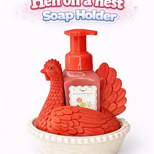 以下が含まれることがあります： 赤い鶏の形をした石鹸ホルダーと、それに合う石鹸ディスペンサー。鶏は白いパイ型の皿の中にあります。「Hen on a nest Soap Holder」というテキストが上に表示されています。