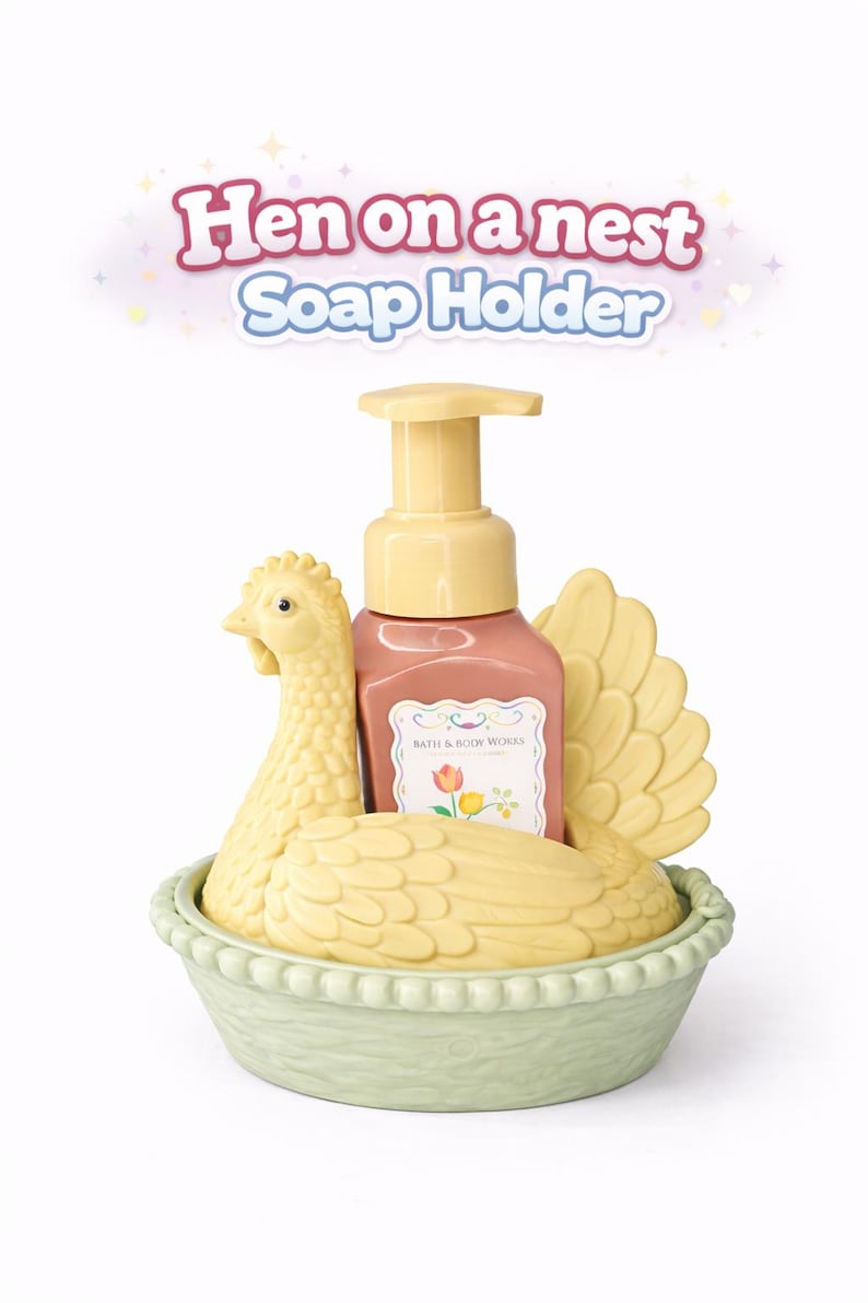 以下が含まれることがあります： 黄色いニワトリの形をした装飾的な石鹸ホルダー。薄緑色のバスケットの中にあります。 花柄のラベルが付いたピンク色の石鹸ディスペンサーが入っています。 テキスト「Hen on a nest Soap Holder」が上に表示されています。