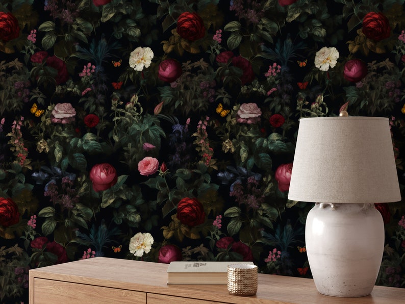 Pu&ograve; includere: Una carta da parati floreale scura con un motivo ripetitivo di fiori rossi, rosa e bianchi, foglie verdi e farfalle. Una lampada in ceramica bianca con un paralume beige &egrave; posizionata su un tavolo di legno davanti alla carta da parati.
