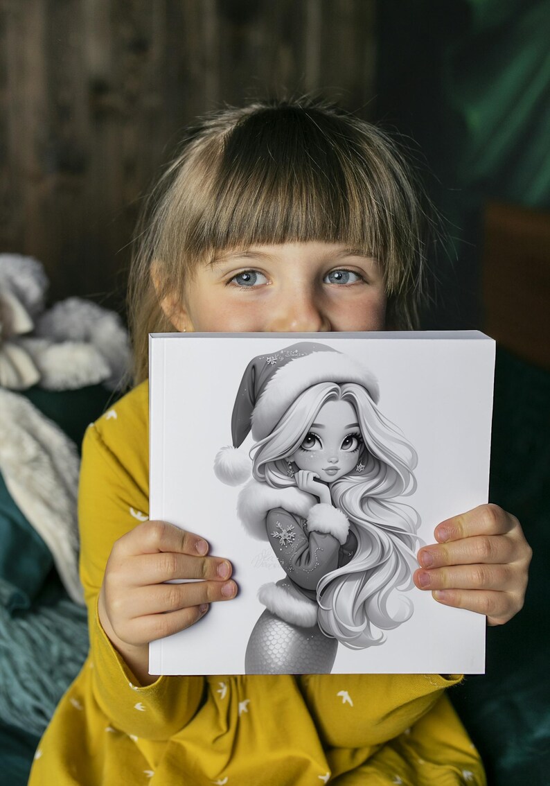 Puede incluir: Una ni&ntilde;a sostiene una ilustraci&oacute;n en escala de grises de una sirena con un gorro de Pap&aacute; Noel y un abrigo con ribete de piel. La sirena tiene el pelo largo y suelto y un copo de nieve en su abrigo. La ni&ntilde;a lleva una camisa amarilla de manga larga.