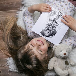 May include: A young girl lies on a white fluffy rug, holding a drawing of a girl with an umbrella and a plaid skirt. The drawing is in black and white and has a whimsical style. A beige teddy bear is lying next to the girl.
