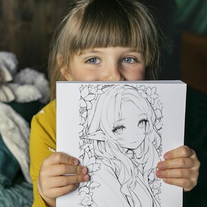Op de afbeelding: Een witte vierkante kunstdruk met een zwart-wit anime-stijl illustratie van een vrouwelijk personage met lang haar, puntige oren en bloemaccenten. De print wordt vastgehouden door een persoon die een gele top draagt.