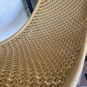 May include: A close-up of a woven hammock chair made of a light brown rope. The chair is made of a tight weave and has a smooth, rounded edge.