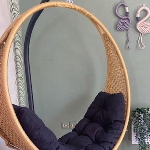 May include: A gold-colored round hanging chair with a black cushion. The chair is made of woven rope and has a metal frame.