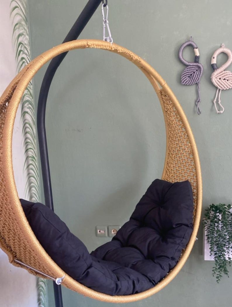 May include: A gold-colored round hanging chair with a black cushion. The chair is made of woven rope and has a metal frame.