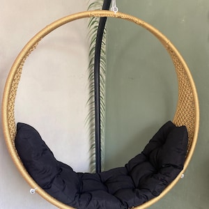 May include: A gold-colored round hanging chair with black cushions. The chair is made of woven rope and has a metal frame.