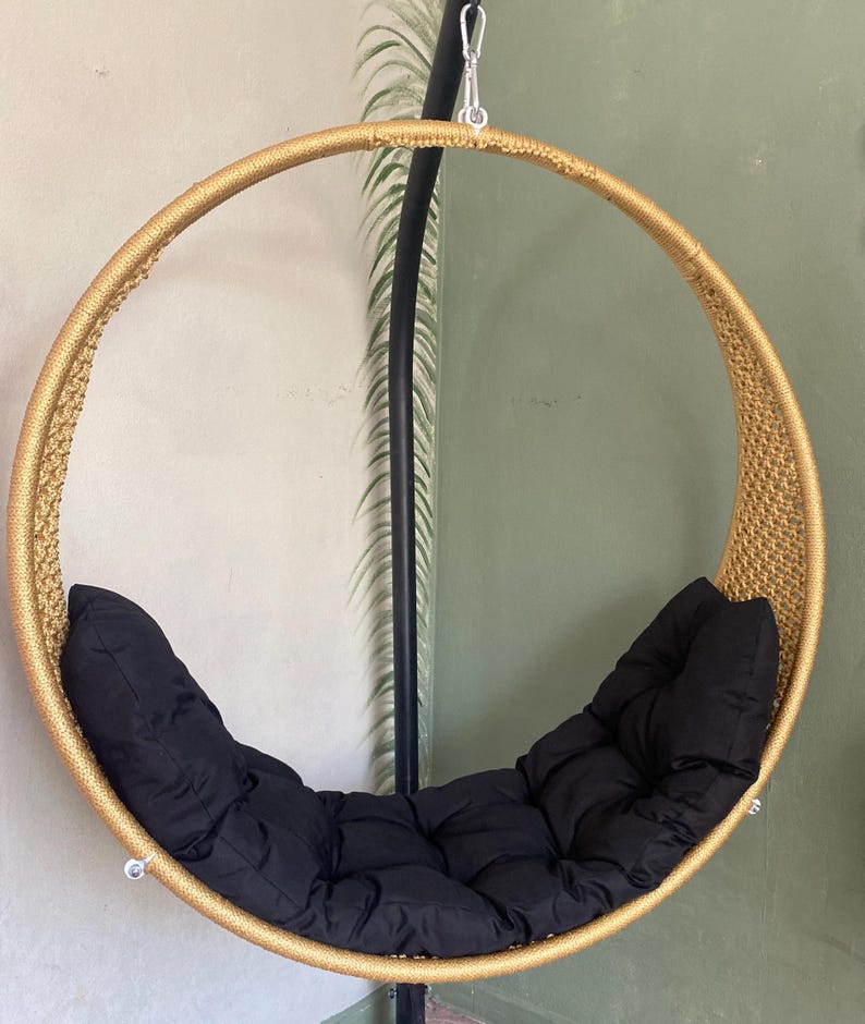 May include: A gold-colored round hanging chair with black cushions. The chair is made of woven rope and has a metal frame.