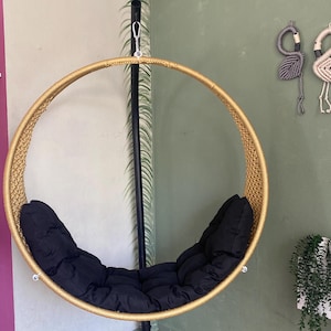 May include: A gold-colored round hanging chair with black cushions. The chair is suspended from a black metal stand.