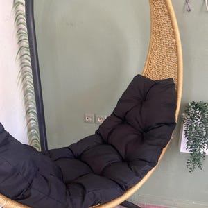 May include: A hanging chair with a black cushion. The chair is made of woven rope and has a gold finish. The chair is suspended from a black metal stand.