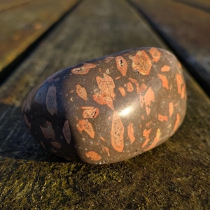 Könnte beinhalten: Nahaufnahme eines braunen und orangefarbenen Steins mit einer glatten, abgerundeten Oberfläche. Der Stein liegt auf einer Holzoberfläche.