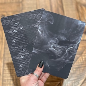 May include: Two black cards with different designs. One card has a pattern of white scales, the other card has a white smoke design.