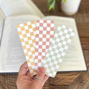 May include: Three checkered bookmarks in yellow, pink, and green. The bookmarks are held in a hand.