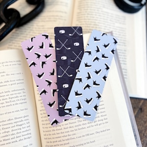 May include: Three different hockey-themed bookmarks. The bookmarks are made of cardstock and feature a variety of hockey-related designs, including hockey sticks, pucks, and skates. The bookmarks are in pink, blue, and black.