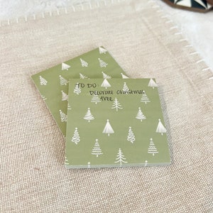 May include: A green notepad with a white Christmas tree pattern. The notepad has a handwritten to-do list that says "To Do: Decorate Christmas Tree".