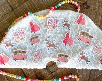 May include: A white fabric surface with various Christmas-themed stickers. The stickers feature a pink and green Christmas tree, a pink van with a Christmas tree on top, a reindeer, and the phrase "Be merry & bright".
