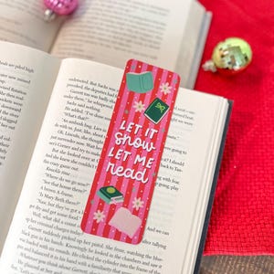 May include: Pink and white striped bookmark with the text "Let it snow let me read". The bookmark features illustrations of books and flowers.