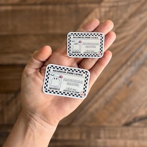 May include: Two rectangular stickers with a black and white checkered border. The stickers read "HALLOWEEN SPOOR LICENSE" and "PROFESSIONAL GHOSTER" with a cartoon ghost illustration. The text "CERTIFIED TO SPOOK" is also present.