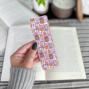 May include: A rectangular bookmark with a pink background and a repeating pattern of Halloween-themed illustrations. The illustrations include pumpkins, ghosts, and the word "Spook".
