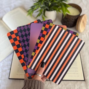 May include: A fan of five rectangular cards featuring distinct patterns including orange and black checkers, purple and black diamonds, a solid purple gradient, a green and orange checkered pattern, and vertical orange, black, and white stripes.