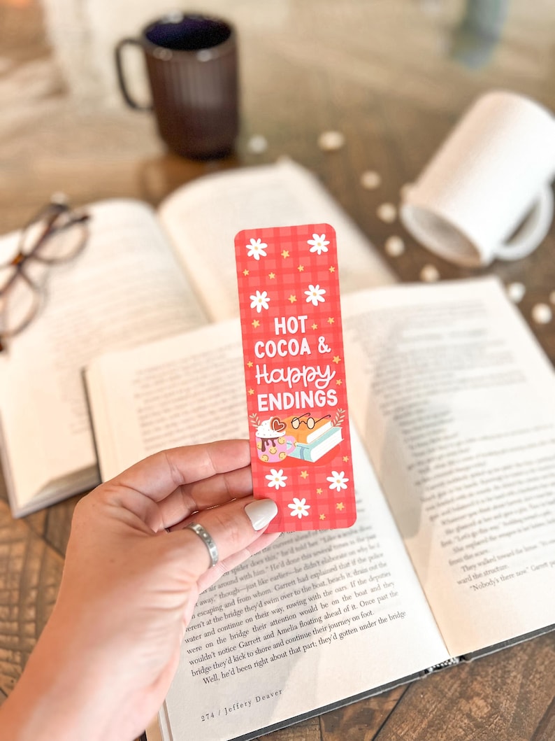 May include: Red and white checkered bookmark with the text "HOT COCOA & Happy ENDINGS" and a cartoon illustration of a person reading a book with a cup of cocoa.