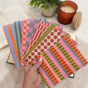 May include: A set of rectangular cards featuring various geometric patterns in vibrant colors including orange, pink, green, and blue. The cards are arranged in a fan shape, displaying designs such as stripes, checkered squares, and grid patterns.