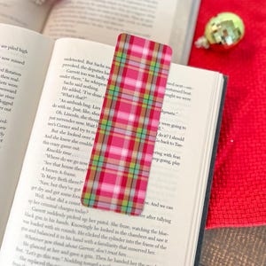 May include: A pink and green plaid bookmark with a red border. The bookmark is made of fabric and has a checkered pattern.