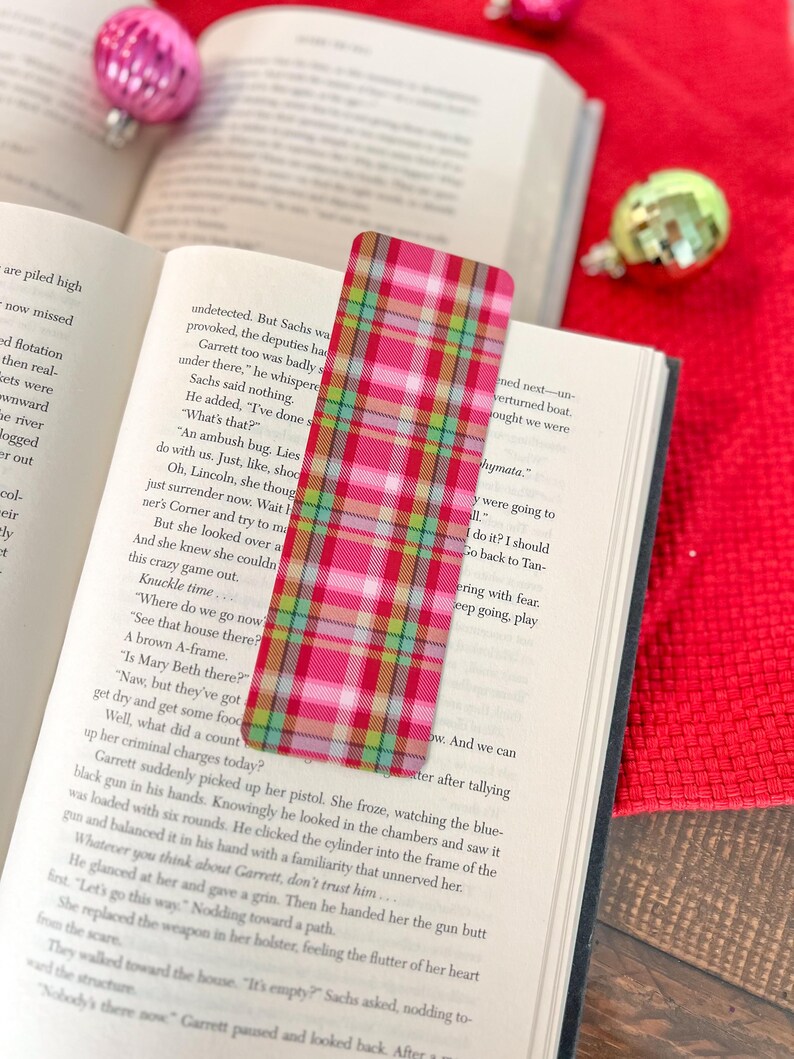 May include: A pink and green plaid bookmark with a red border. The bookmark is made of fabric and has a checkered pattern.