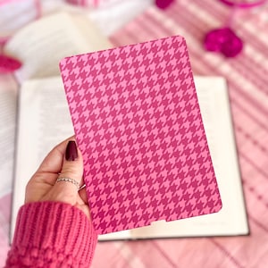 May include: A pink and white houndstooth patterned bookmark. The bookmark is held in a hand wearing a pink sweater.