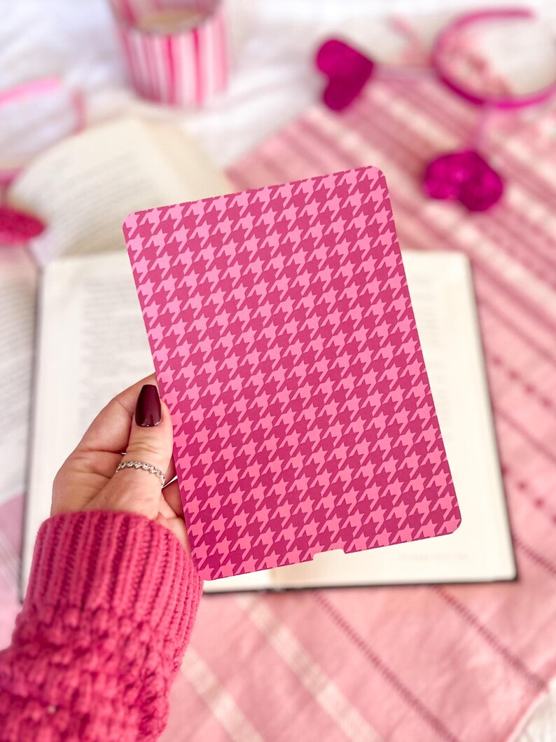 May include: A pink and white houndstooth patterned bookmark. The bookmark is held in a hand wearing a pink sweater.
