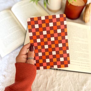 Pu&ograve; includere: Una carta rettangolare caratterizzata da un motivo a scacchi ripetuto nei toni dell'arancione, rosso, marrone scuro e bianco. La griglia &egrave; composta da piccoli quadrati uniformi disposti in uno schema coerente e alternato su tutta la superficie.