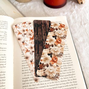Op de afbeelding: Drie decoratieve bladwijzers met bloemen- en houtnerfdesigns liggen op een open boek. De bladwijzers hebben een mix van cr&egrave;me, bruine en oranje bloempatronen en een centrale bladwijzer met een houtnerftextuur.