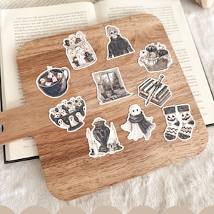 May include: A wooden cutting board displays a collection of Halloween-themed stickers. The stickers feature ghosts, pumpkins, a skull, and other spooky illustrations. The text at the bottom says, "Look for the rest of the collection!"