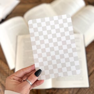 May include: A rectangular card featuring a repeating checkerboard pattern in alternating shades of light beige and white. The card has rounded corners and a smooth, flat surface, displaying a consistent grid design across the entire front face.