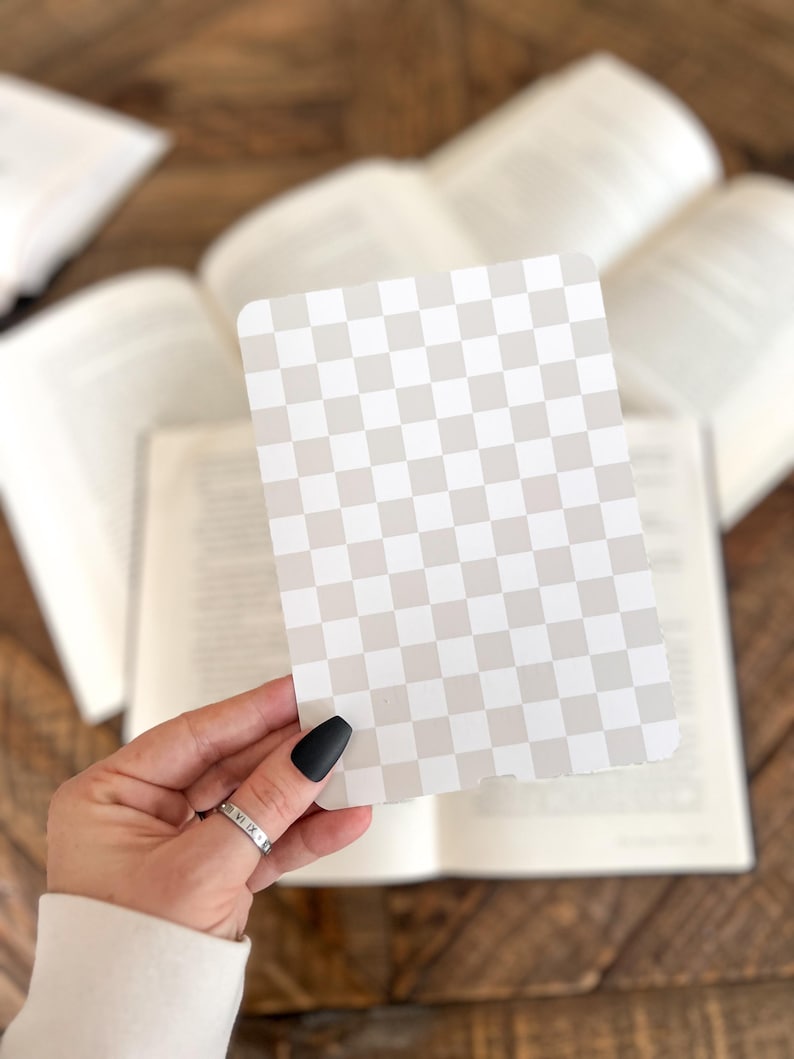 May include: A rectangular card featuring a repeating checkerboard pattern in alternating shades of light beige and white. The card has rounded corners and a smooth, flat surface, displaying a consistent grid design across the entire front face.