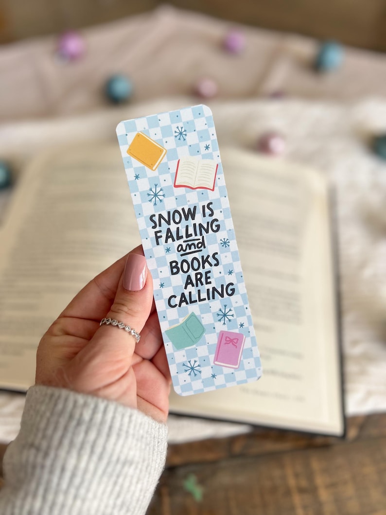 May include: A blue and white checkered bookmark with the text "SNOW IS FALLING and BOOKS ARE CALLING". The bookmark features illustrations of books with snowflakes.