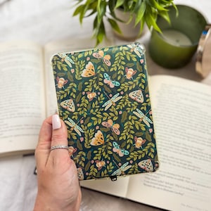 May include: A clear protective tablet case featuring a dark green background with a repeating pattern of various moths, butterflies, and dragonflies nestled among dense green leaves and small pink flowers, designed to fit a rectangular electronic device.