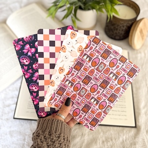 May include: Four rectangular bookmarks featuring distinct patterns: one with pink pumpkins and bows on black, one with a pink and orange checkerboard, one with ghost and pumpkin ice cream cones, and one with a grid of Halloween icons and the word SPOOKY.