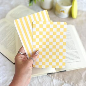May include: Two rectangular cards with rounded corners. One card features a pattern of vertical yellow and white stripes, while the other card displays a yellow and white checkered pattern. Both cards are held together in a stack.