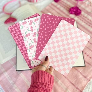 May include: Four pink patterned cards with different designs. The cards feature a checkered pattern, a pattern of small hearts, a pattern of cherries, and a houndstooth pattern.